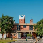 #PraTodosVerem: A foto mostra a fachada de um prédio de tijolos à vista com o letreiro UNIVALI no topo, rodeado por árvores, gramado e carros estacionados.